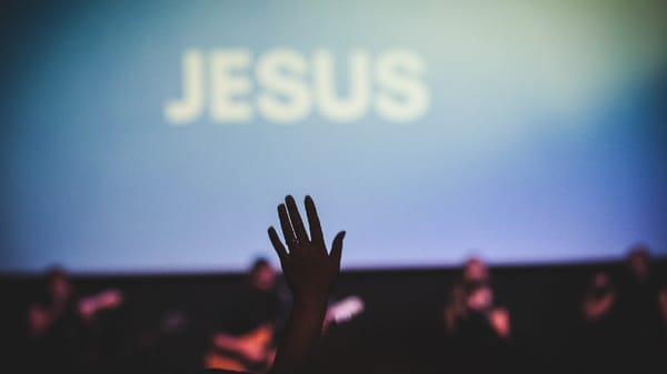 hand in the air, the "Jesus" is on the screen; Article: 20 Songs To Perform This Easter